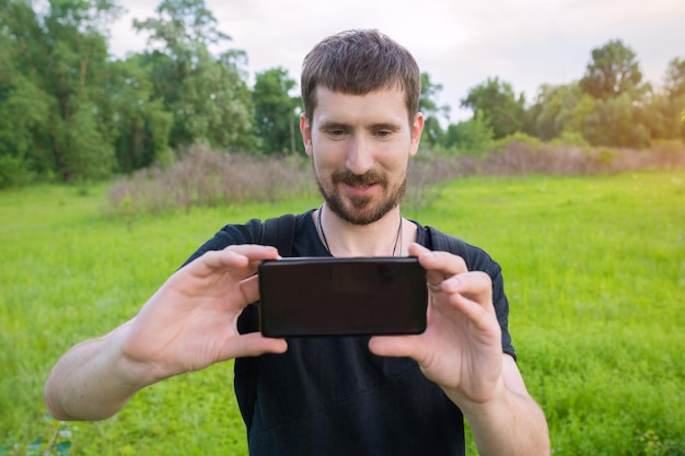 A young man in the park takes pictures on the phone and blogs on social networks