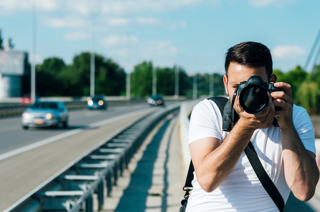 Молодой человек фотограф снимает с камеры DSLR на открытом воздухе