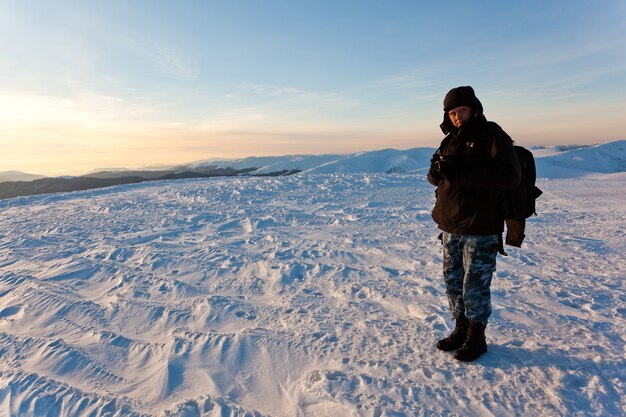 Молодой человек-фотограф в зимней одежде стоит и делает фото с камерой