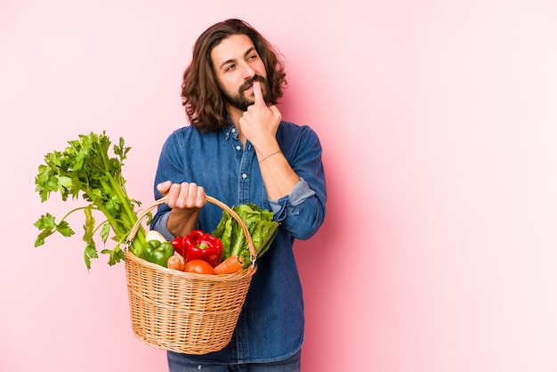 Young man picking organic vegetables from his garden isolated relaxed thinking about something looking at a copy space.