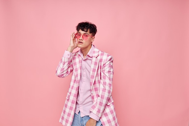 A young man pink glasses checkered jacket fashion posing pink background unaltered