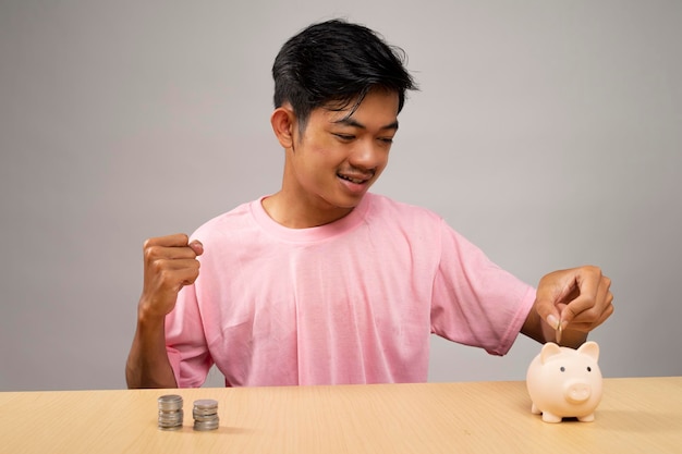 ピンクのシャツを着た若い男がコイン貯金の概念で貯金箱にお金を入れます