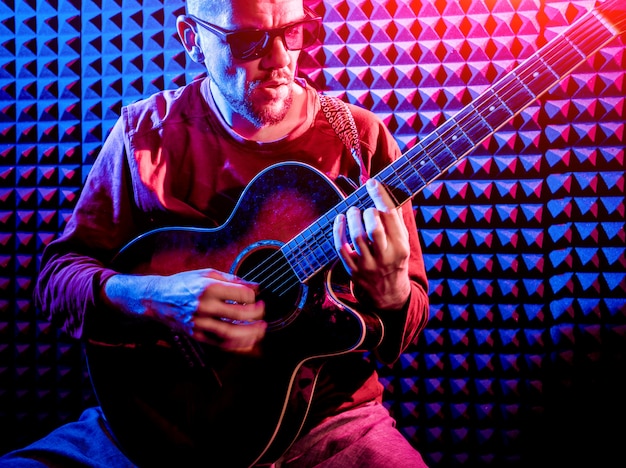 Young man playing on the acoustic guitar in sound recording studio.