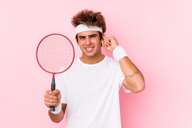 Young man playing badminton isolated covering ears with hands.