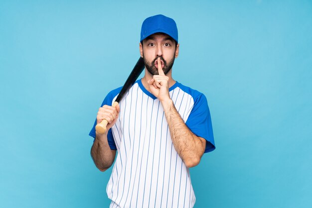 Young man playing baseball over isolated blue showing a sign of silence gesture putting finger in mouth