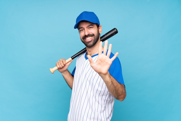 Young man playing baseball over isolated blue wall counting five with fingers