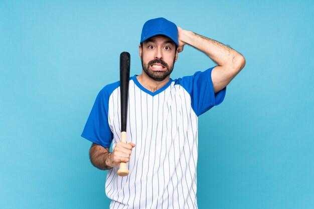 Young man playing baseball over isolated blue wall frustrated and takes hands on head