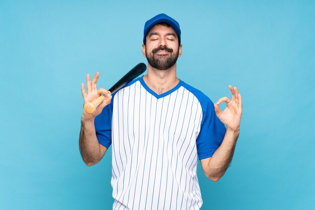 Young man playing baseball over isolated blue in zen pose