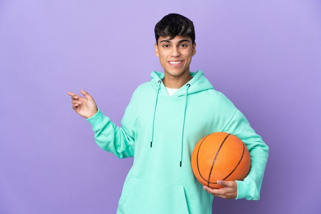 Young man playing basketball over isolated purple background\
pointing finger to the side