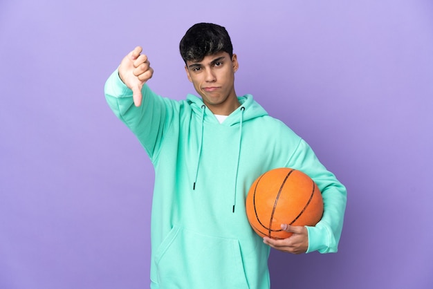 Young man playing basketball over isolated purple background
showing thumb down with negative expression