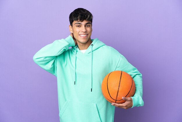 Young man playing basketball on isolated purple laughing