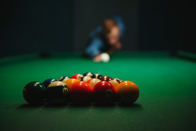 Young man playing billiards in the dark billiard club