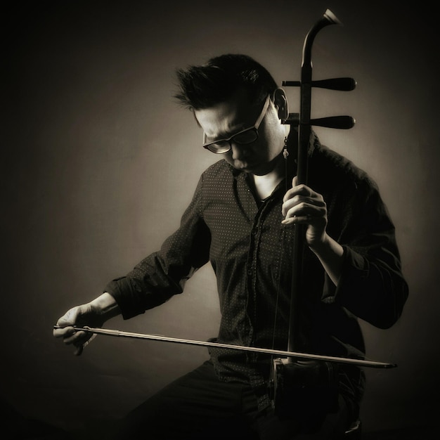 Photo young man playing erhu against gray background