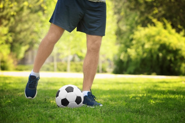 公園の緑の芝生でサッカーをしている若い男