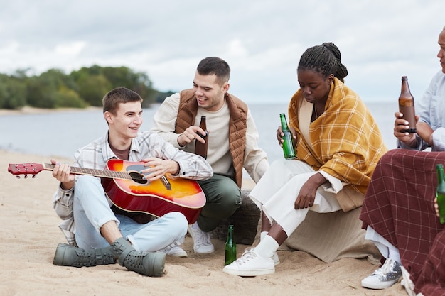 Giovane che suona la chitarra alla festa in spiaggia