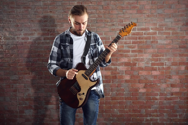 Young man playing guitar on brick wall background