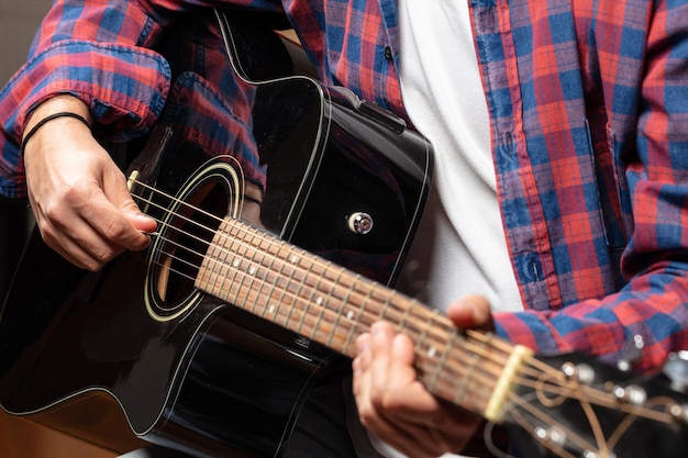 Young man playing guitar close up view dark background