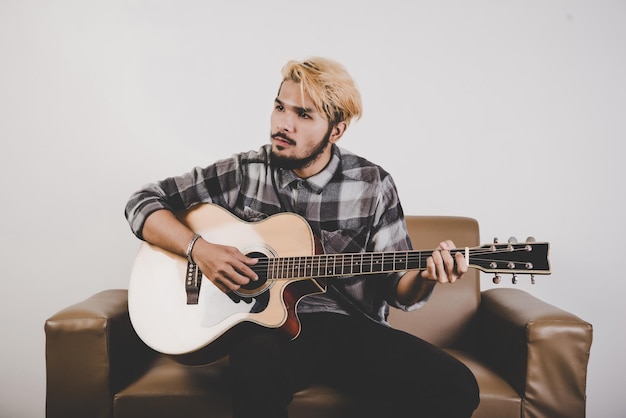 Фото Молодой человек играет на гитаре, сидя на кресле на белом фоне