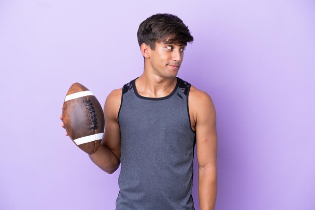 Young man playing rugby isolated on purple background looking to the side