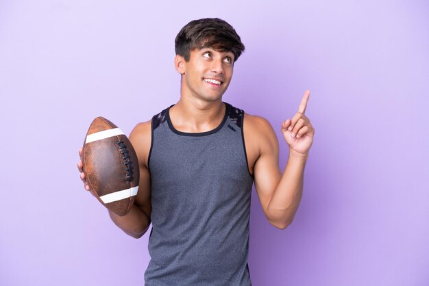 Young man playing rugby isolated on purple background pointing up a great idea