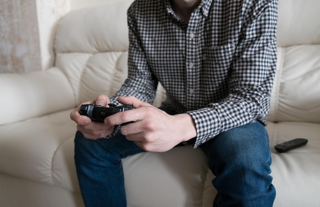 Молодой человек играет в видеоигры с джойстиком и сидит на диване