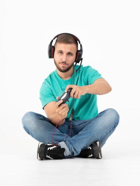 Giovane che gioca ai videogiochi con un controller e una cuffia su uno sfondo bianco con jeans, scarpe nere e maglietta verde