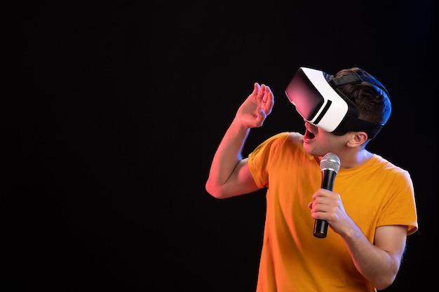 Young man playing virtual reality and singing on dark surface