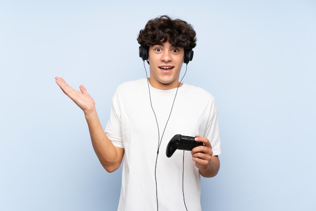 ショックを受けた表情で分離された青い壁を越えてビデオゲームコントローラーで遊ぶ若い男