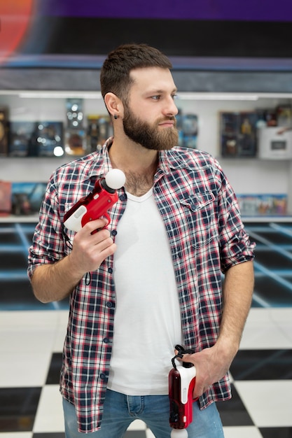 Молодой человек играет на приставке, эмоциональный геймер снимает игру с помощью контроллера оружия и улыбается.