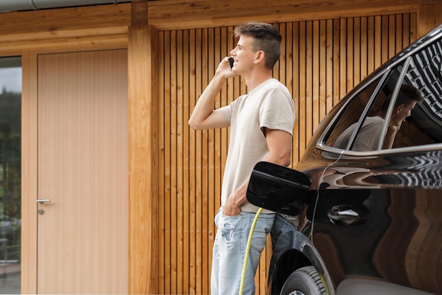 Young man plugging a charger in electric car at modern house home