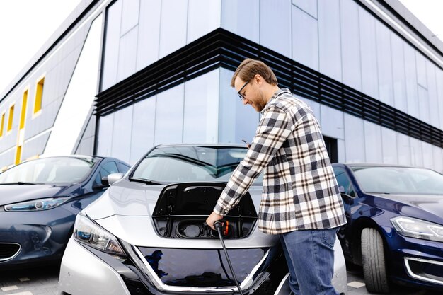 Young man plugging charging cable into the car socket Electric car charging concept