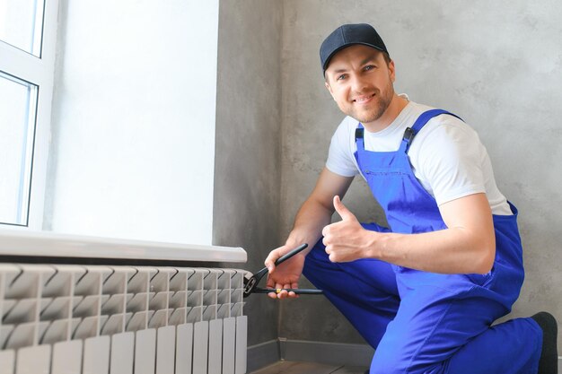 young man plumber checking radiator while installing heating system in apartment