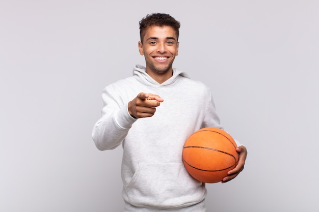 Young man pointing at front with a satisfied, confident, friendly smile, choosing you. basket concept