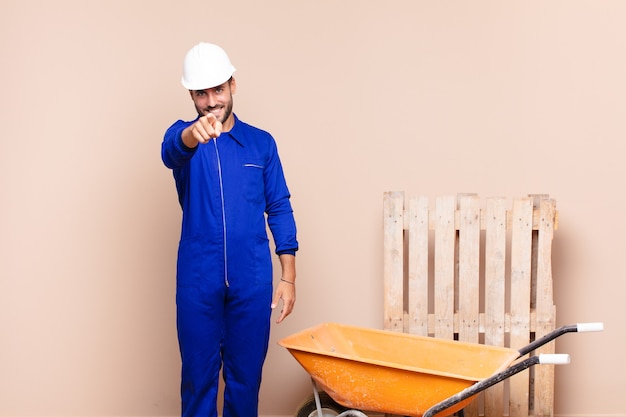 Young man pointing at front with a satisfied, confident, friendly smile, choosing you construction concept