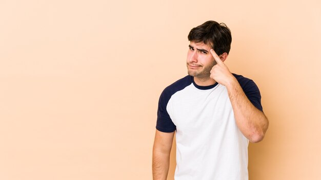 Young man pointing temple with finger, thinking, focused on a task.