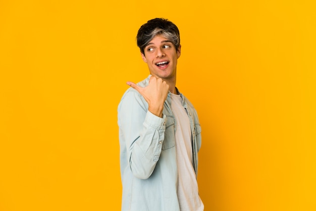 Young man points with thumb finger away, laughing and carefree