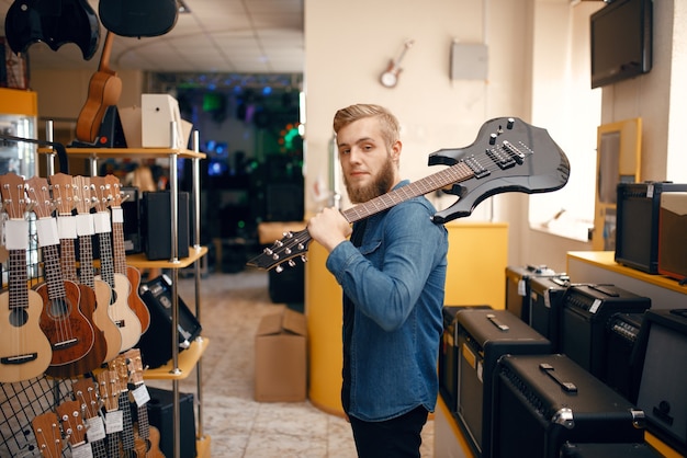 Young man poses with electric guitar on his shoulder in music store.