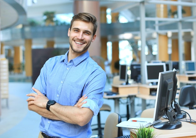 Giovane uomo in posa fiducioso e positivo in un ufficio professionale sul posto di lavoro con spazio