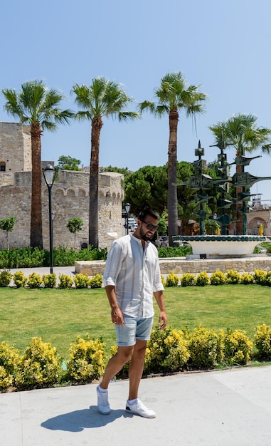 Молодой человек позирует перед замком и садами города Чешме, Турция.