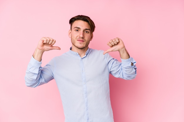 Young man posing in a pink wall isolated feels proud and self confident