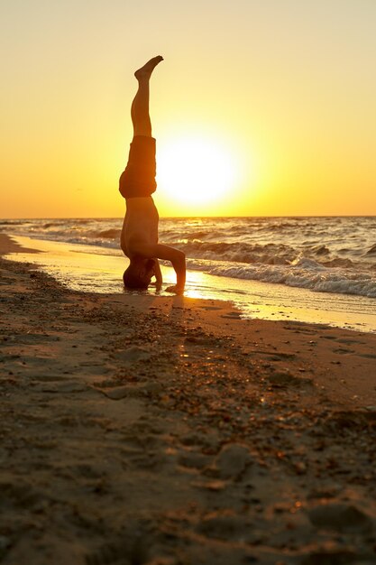 Young man practice balance asana on summer yoga session on beautiful golden beach of tropical island