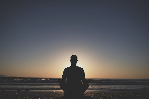 Young man practice yoga on the beach at sunset.