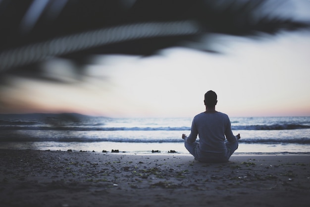 Young man practice yoga on the beach at sunset.