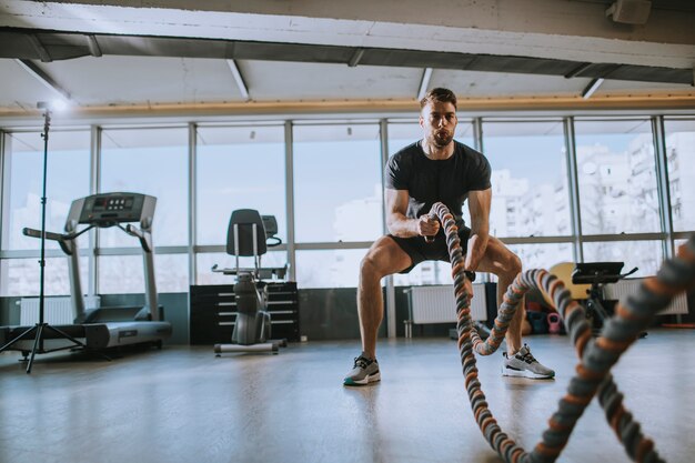 Young man practicing with battle ropes in the gym