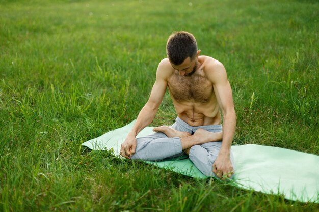Молодой человек занимается йогой на зеленой траве в парке. Медитация. Пресс