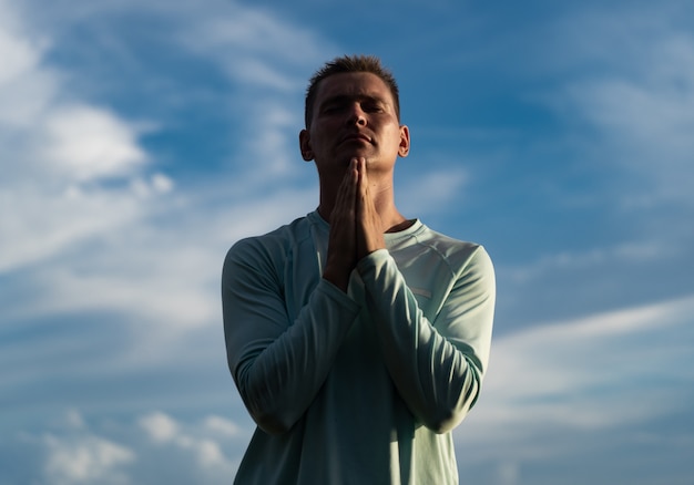 Young man pray on blue sky background religion faith and hope concept