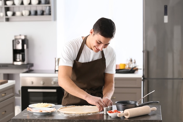 Young man preparing dough for pizza at table