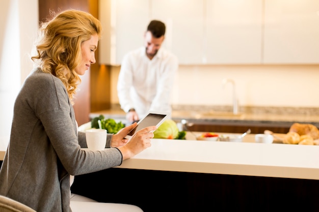 Young man preparing a meal while a young woman uses tablet in a modern kitchen