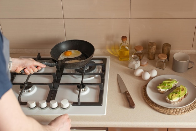 Young man preparing toast with avocado and egg for breakfast in the kitchen