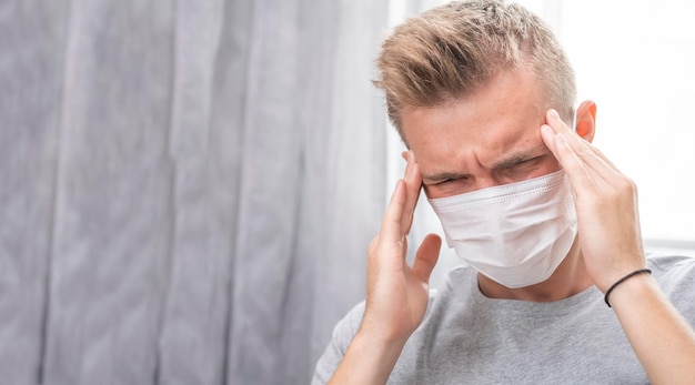 Young man in a protective mask holds his head with his hands Man has a headache Copy space